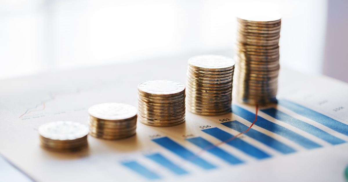 The image centres on a row of small stacks of coins, in increasing heights from left to right. They are sat on top of a sheet of paper, which displays a bar chart.