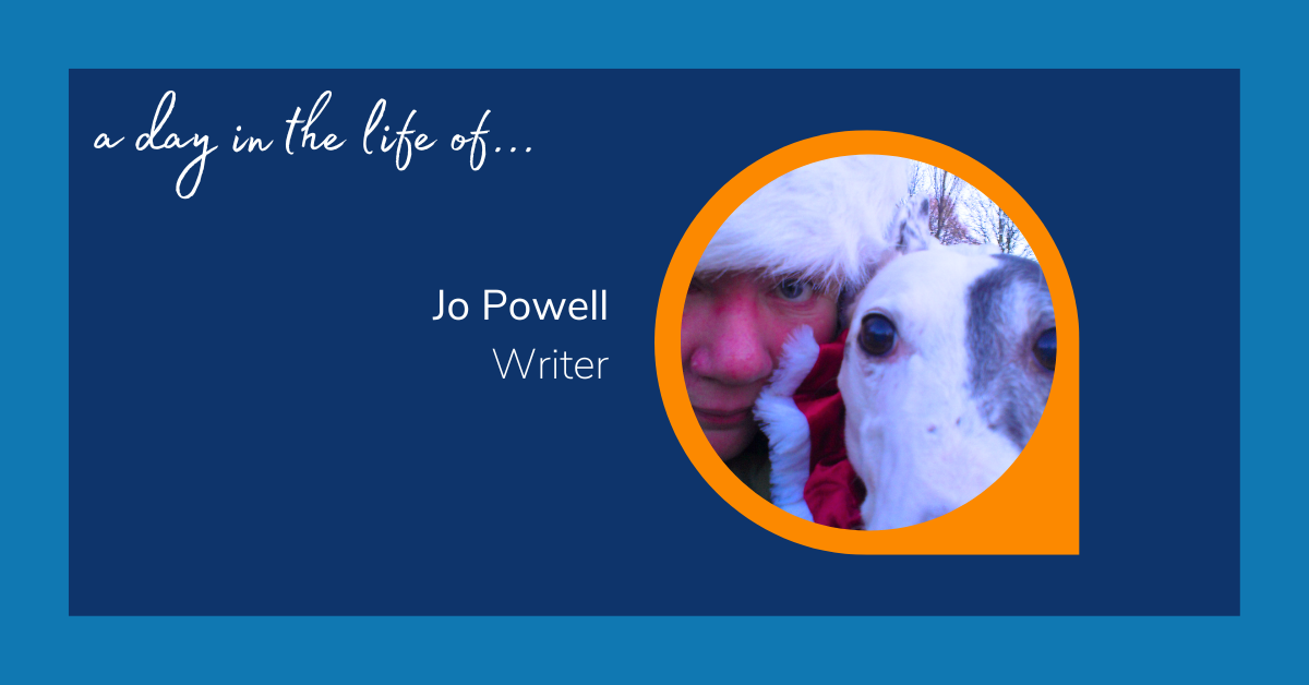 Image reads: "A day in the life of... Jo Powell: Writer. The text is accompanied with an image of a woman, wearing a Santa hat. She is accompanied with a small dog, who appears to also be wearing a Santa costume.