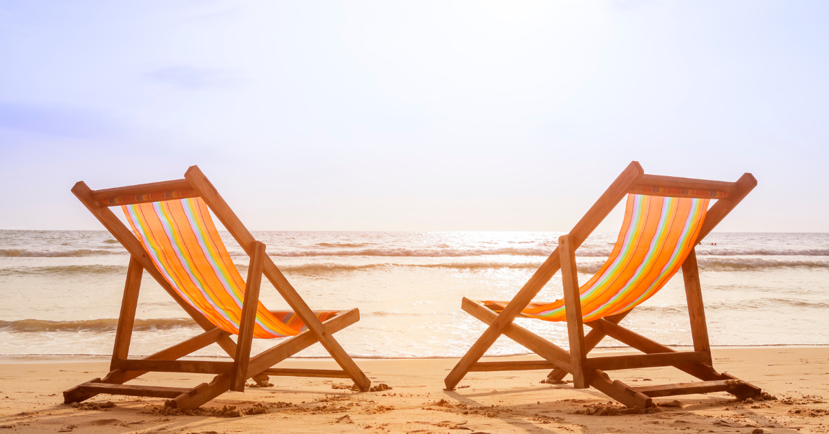 A pair of orange striped deckchairs sit next to each other on the beach at sunset, in front of a calm ocean.