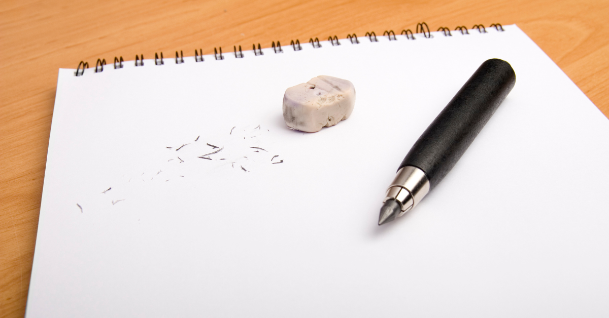 A pen, small rubber, and scattering of rubber dust sit on top of an open, spiral-bound notebook.