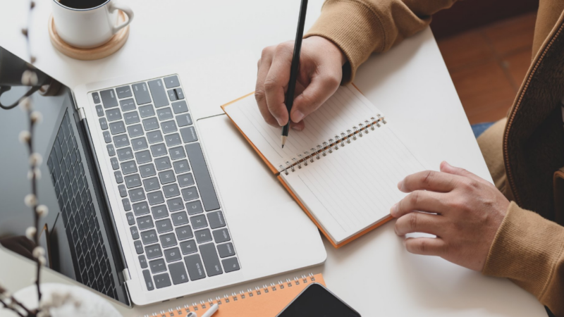 Taking notes next to laptop