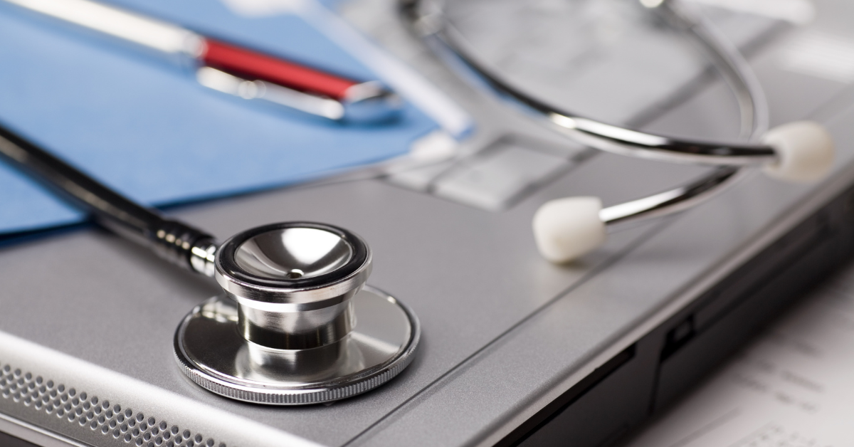 A stethoscope, notebook and pen sit on top of a closed grey laptop