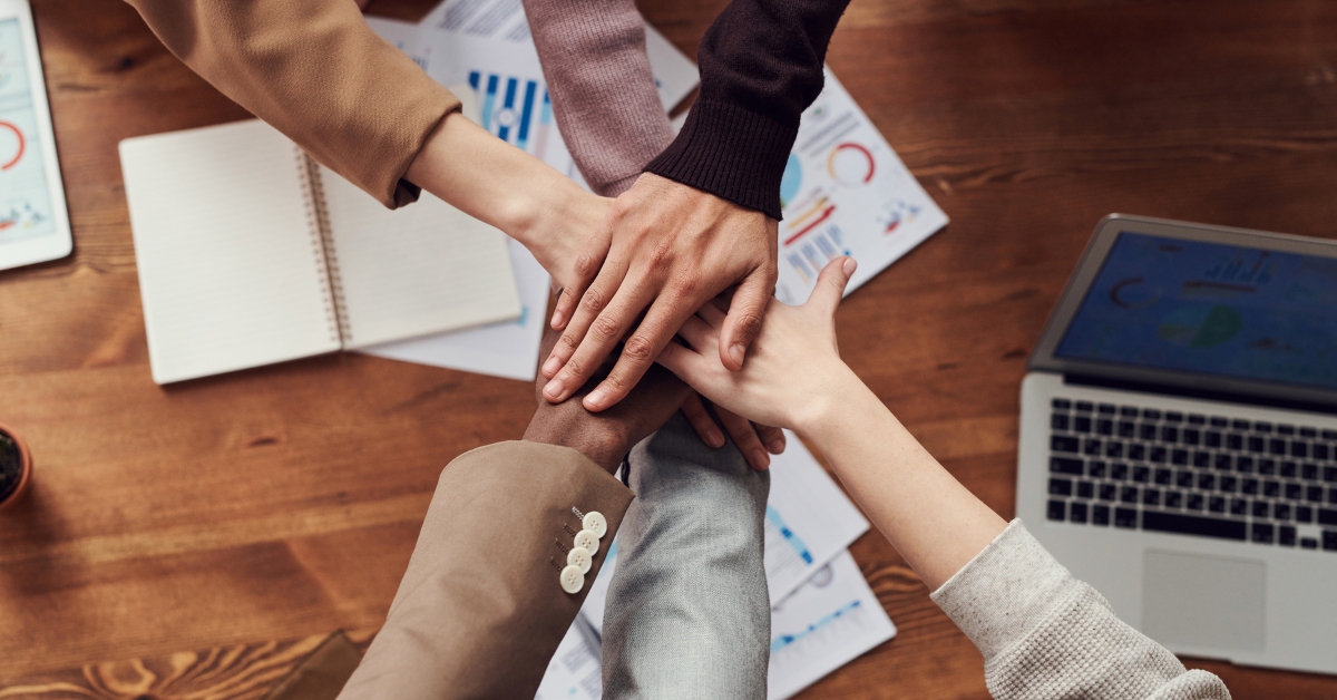 From a bird's eye view, we see six hands overlapping each other in a teamwork pose.