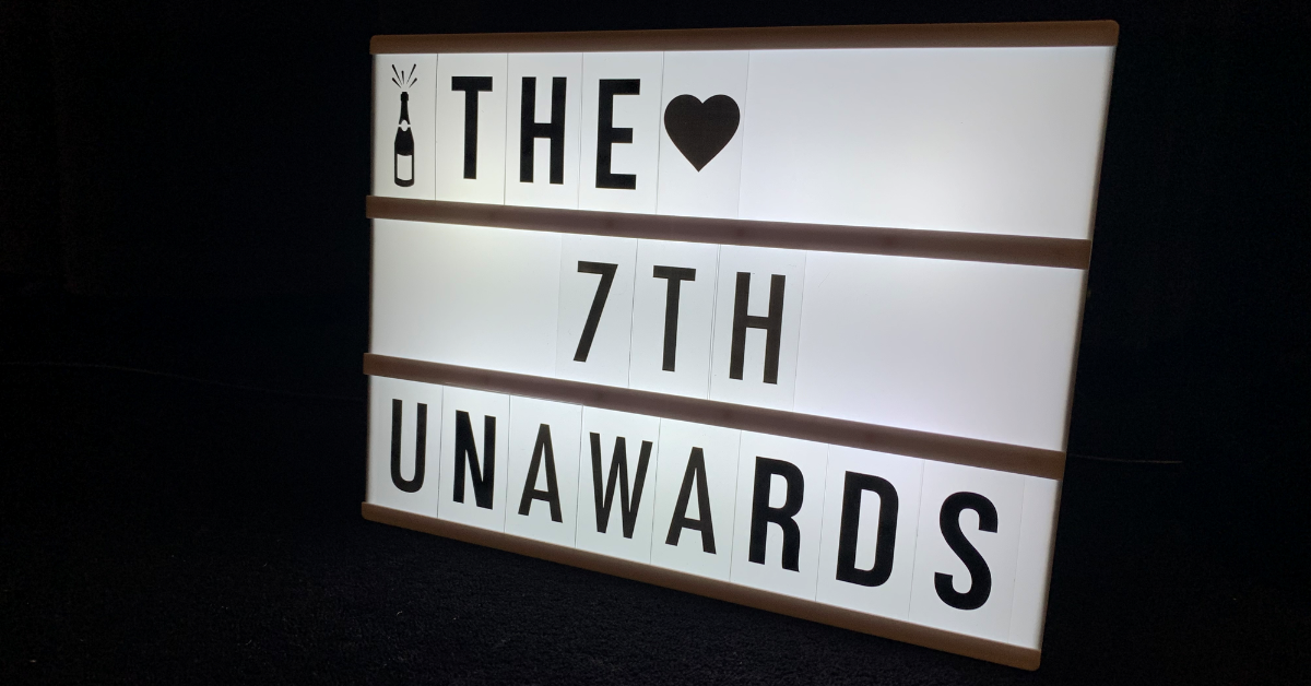 A light-up message board sits in the centre of the image. It reads, in black capital letters: "The 7th Unawards".