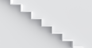 A white minimalist staircase, viewed from side-on, against a white wall.